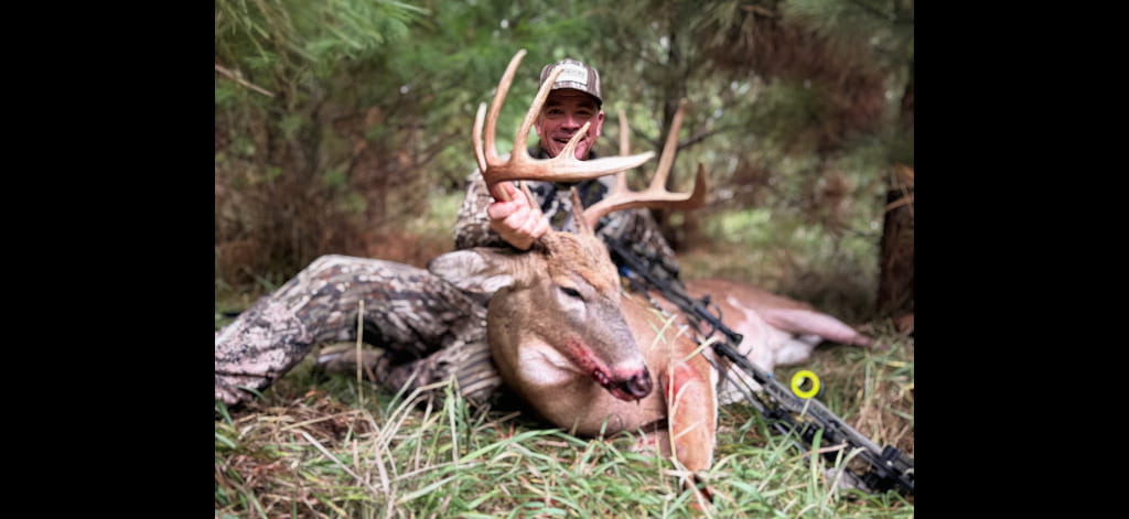 Hunter posing with a harvested white-tailed buck in a wooded Wisconsin habitat.